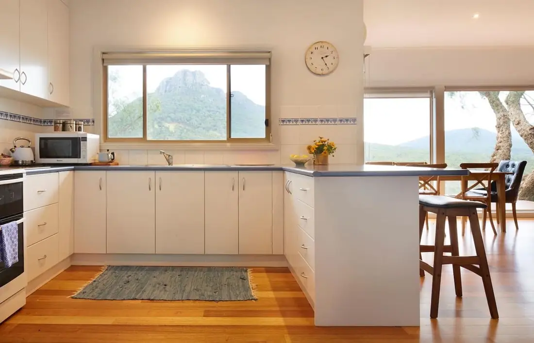 Fully equipped white kitchen with timber floors and a mountain view from the window