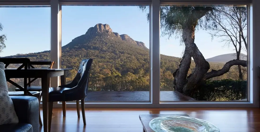 Dining table and armchairs looking out through full-height glass to Mount Sturgeon